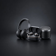 A set of black wireless earbuds with a charging case, a black over-ear headset, and a cylindrical speaker, arranged on a dark gray studio background.