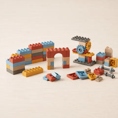 A set of colorful wooden building blocks arranged on a light beige surface, including a long arch, a small tower with gears, and loose pieces scattered in front.