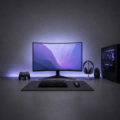 A curved gaming monitor centered on a desk with a keyboard, mouse, headset, game controller, and PC tower, set in a dark room with blue ambient lighting.