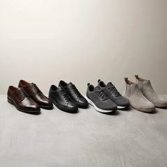Six pairs of casual footwear arranged in a row against a neutral studio backdrop: two dark brown oxford shoes, two black lace-up sneakers, two gray athletic sneakers, and two light gray ankle boots.