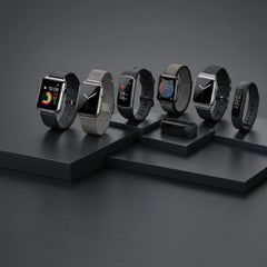 Six smartwatches in various strap colors and styles are displayed on a dark gray geometric platform against a dark gray background.