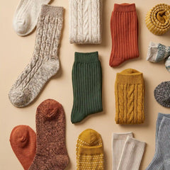 An assortment of cozy knit socks in various colors and textures, including cable knit, ribbed, and spotted patterns, arranged in a flat lay on a warm beige background.