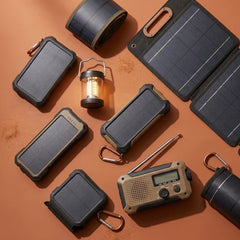 A curated flat-lay of outdoor survival and camping gear on a warm terracotta background, including multiple solar power banks, a lantern, a portable radio, and cylindrical solar pouches.