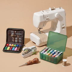 A sewing kit set arranged on a warm beige studio background, including a white sewing machine, a green case filled with thread spools, a black zip case with embroidery floss and tools, a small white and green manual thread cutter, a wooden-handled awl, and a single spool of thread.